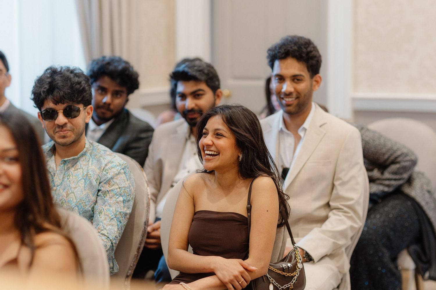Smiling guests at an Indian wedding reception, dressed in elegant attire, enjoying a joyful celebration indoors.