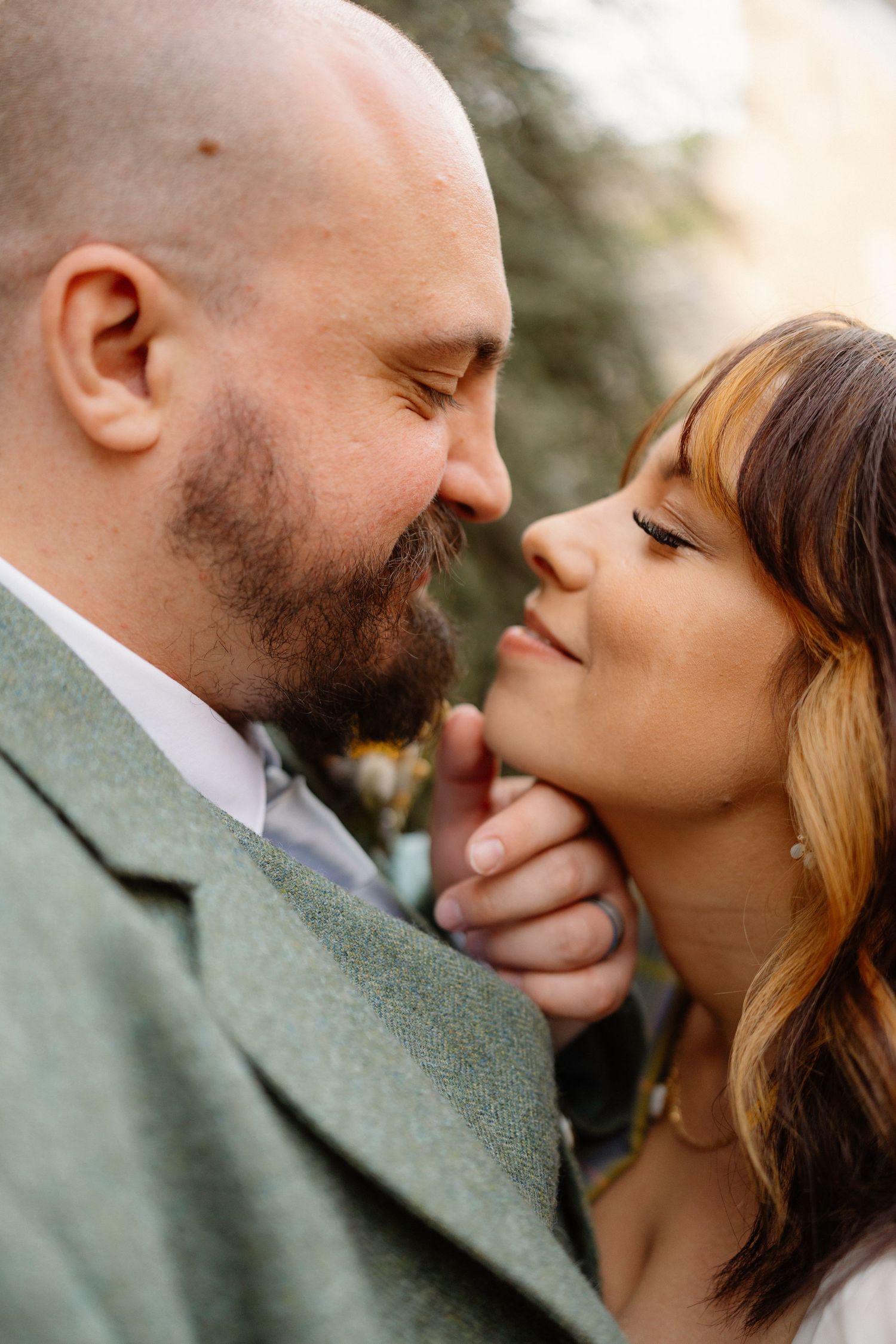 Close-up of a bearded groom in a green suit leaning in to kiss his bride in a tender wedding moment.