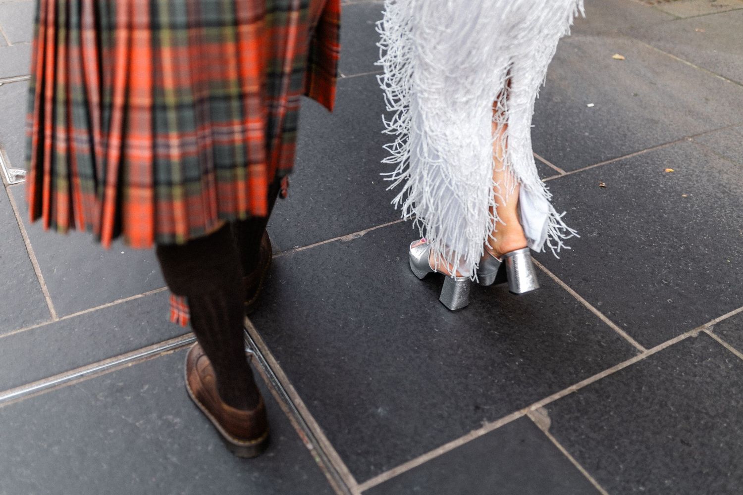 Traditional Scottish tartan kilt and white wedding dress details shown on a cobblestone street.