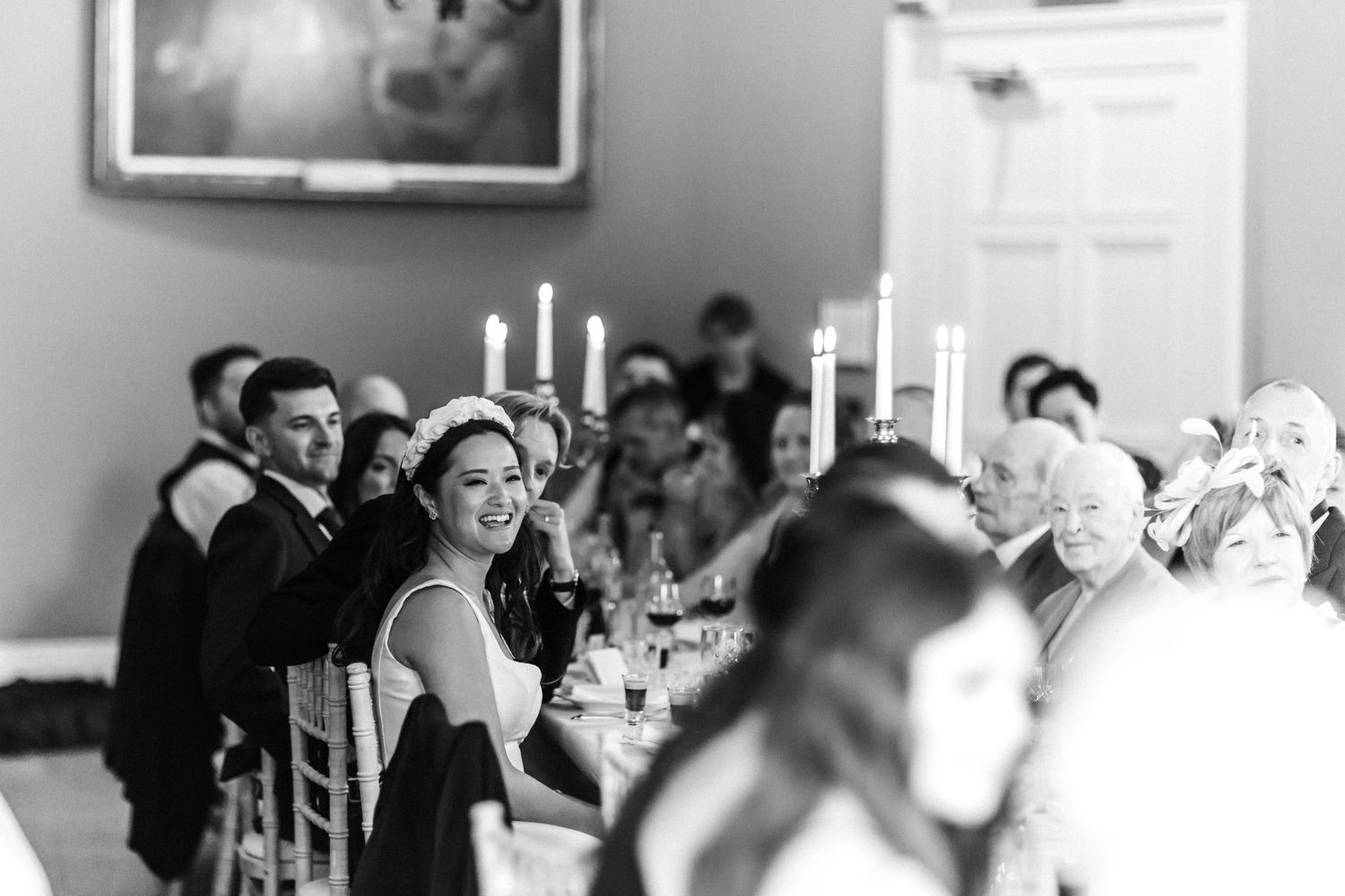 Black and white panoramic view of wedding reception guests at candlelit tables.