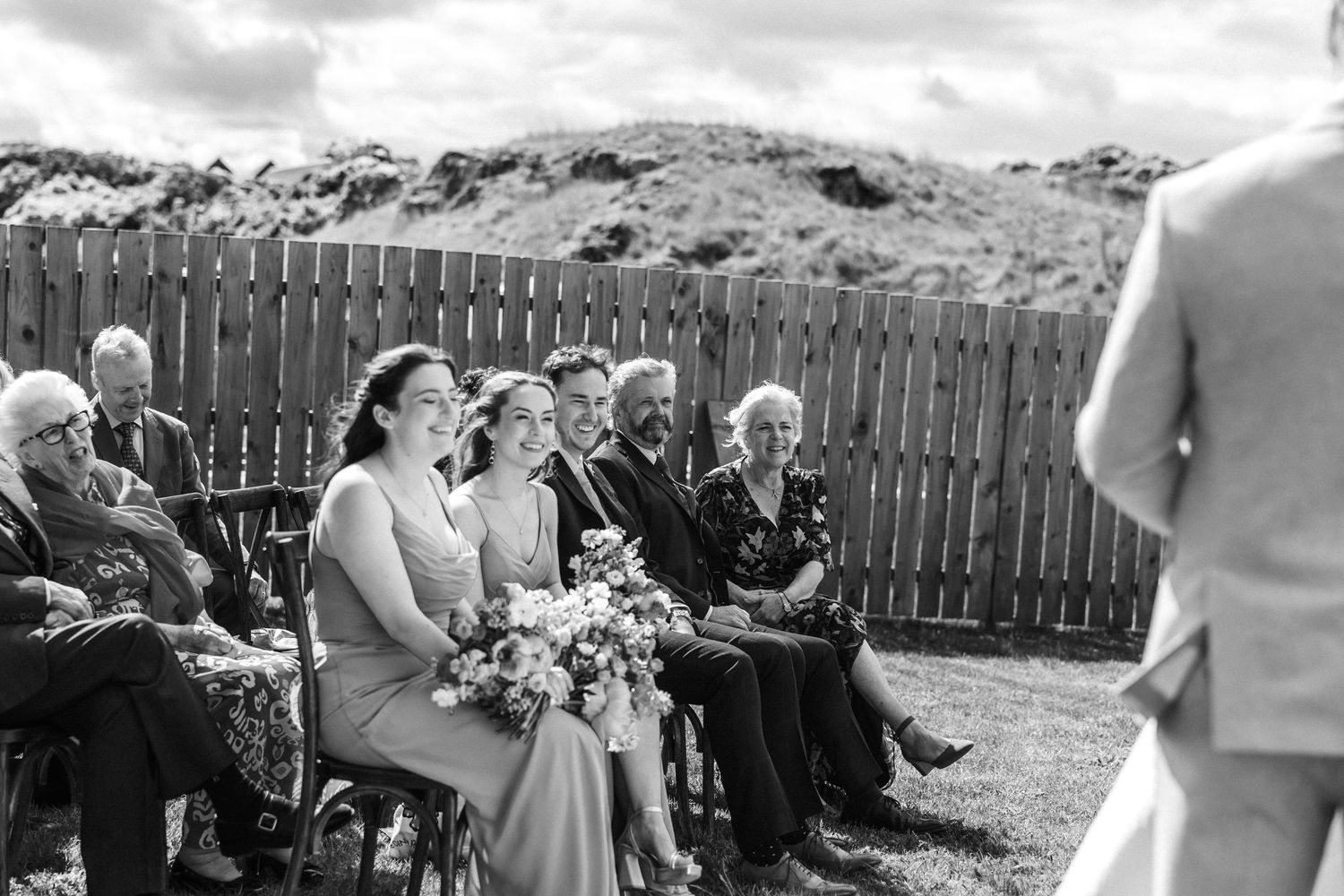 Black and white image of wedding guests seated in rows during an outdoor ceremony.
