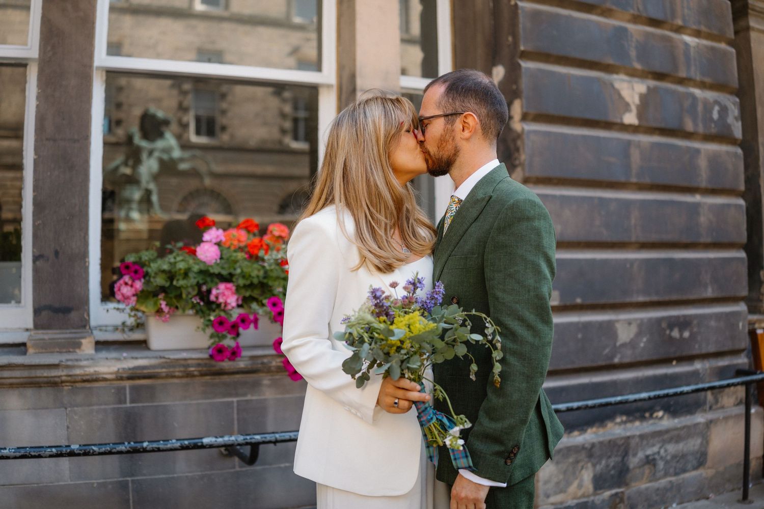 Romantic couple shares tender moments outside a historic stone building with flowers.