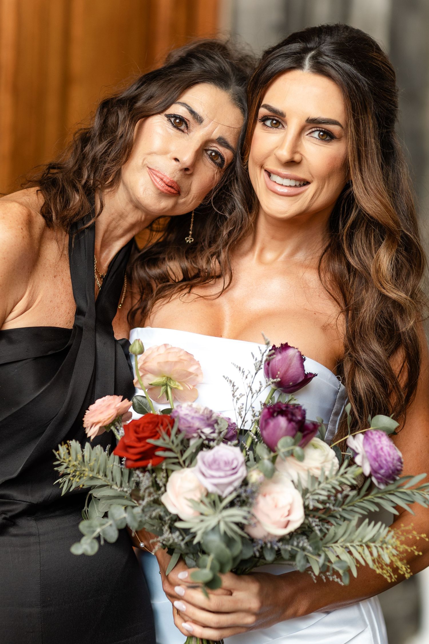Wedding bouquet with purple and red roses held against white dress.