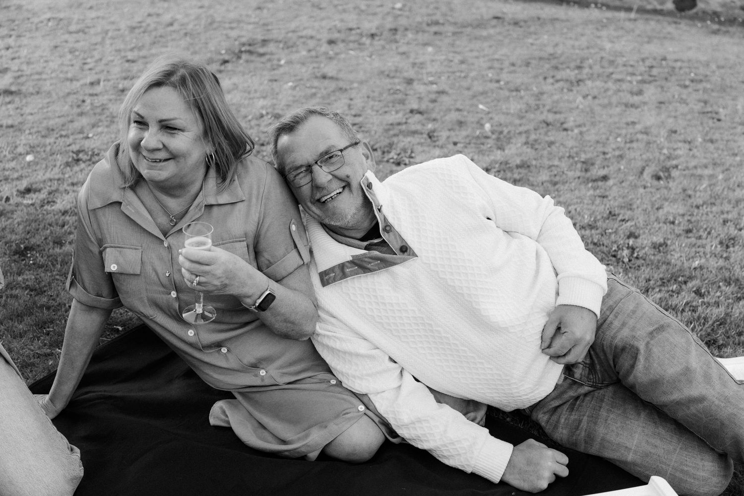 Two people sharing laughter while relaxing on a blanket outdoors in black and white.