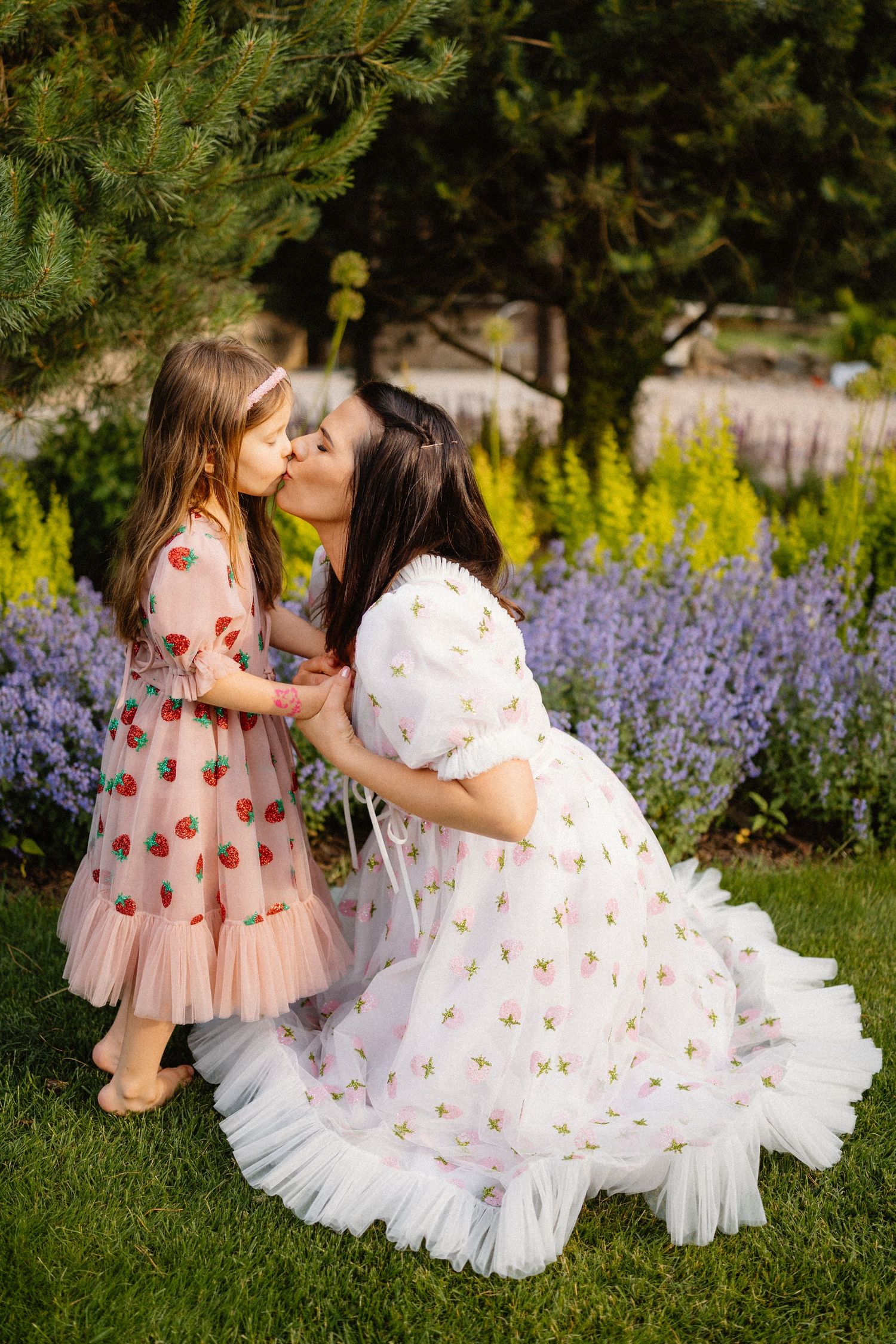 Two flowing dresses with floral patterns dancing together on grass near purple flowers.