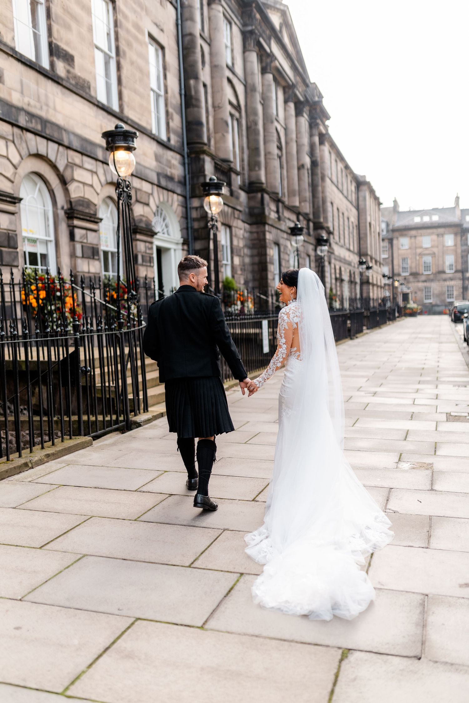 Wedding couple walking along historic stone buildings on cobblestone street.