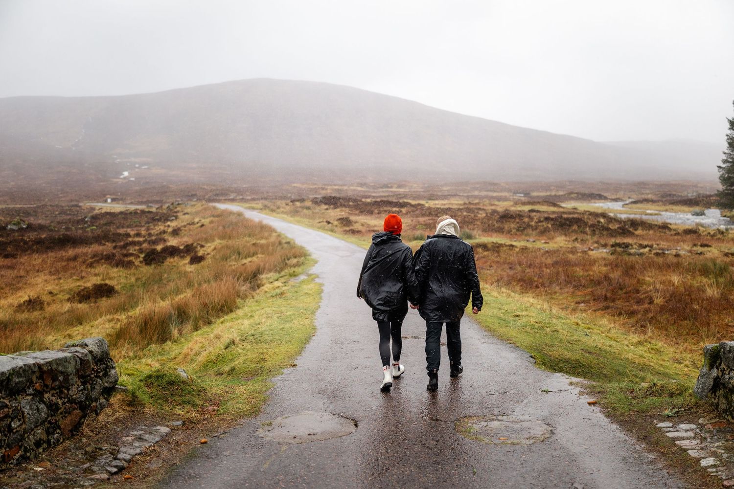 Two people walking together on a wet path through Scottish highlands.