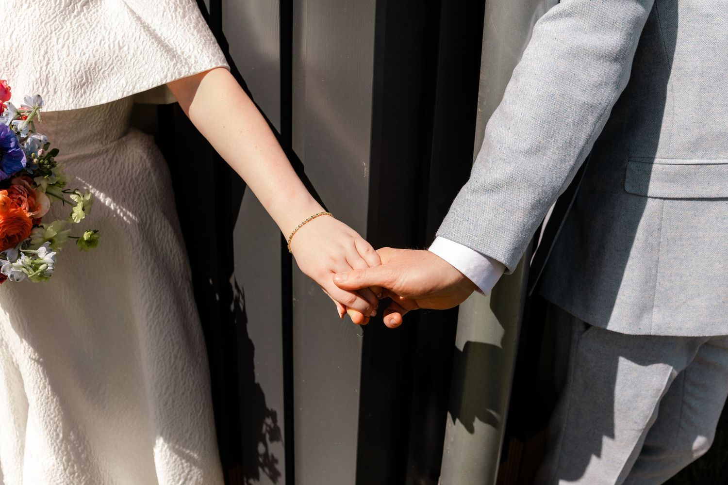 Bride and groom holding hands, bride holding colorful bouquet, groom in gray suit.