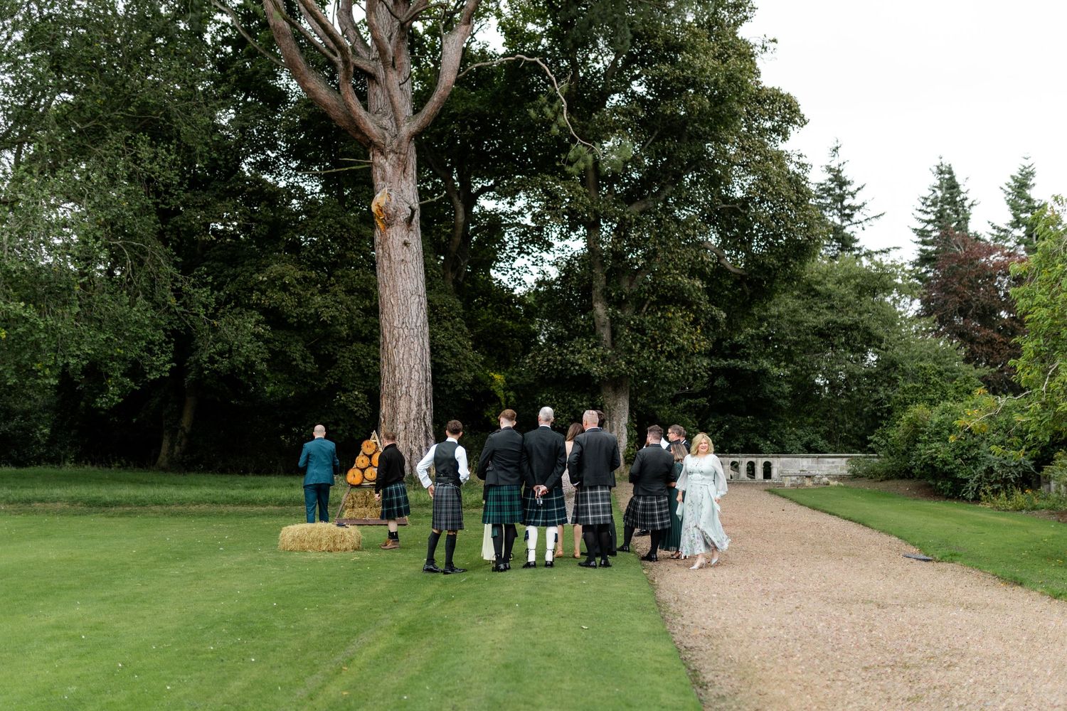 Wedding guests gathering outdoors on gravel path surrounded by lush green trees at a Scottish estate celebration.