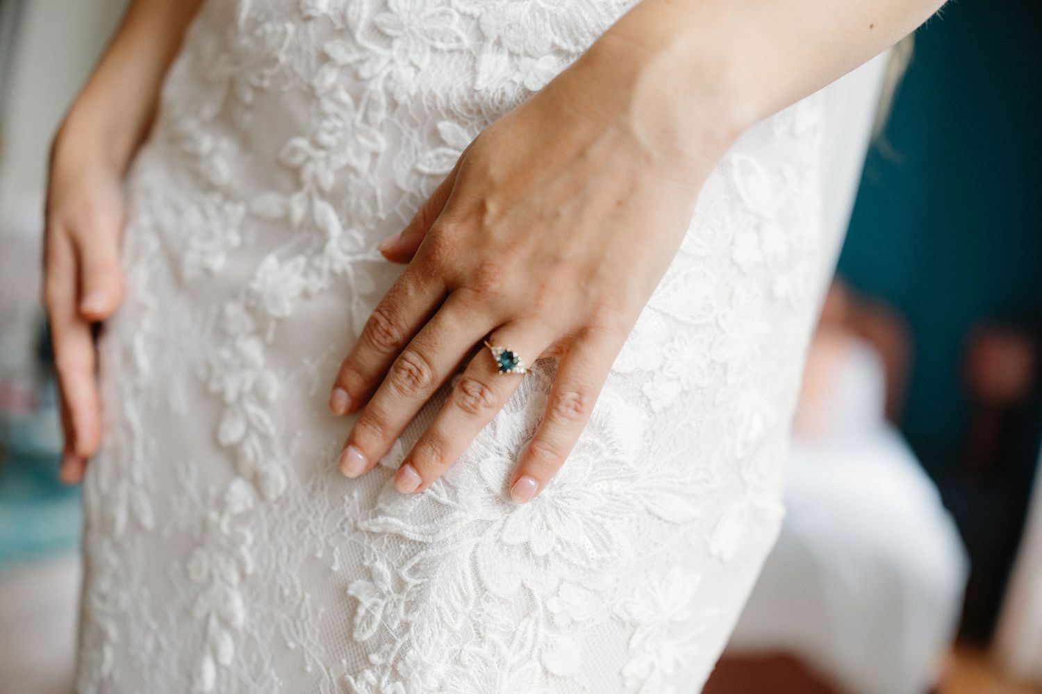 Close-up of bride's hand with sapphire engagement ring resting on white lace wedding dress.