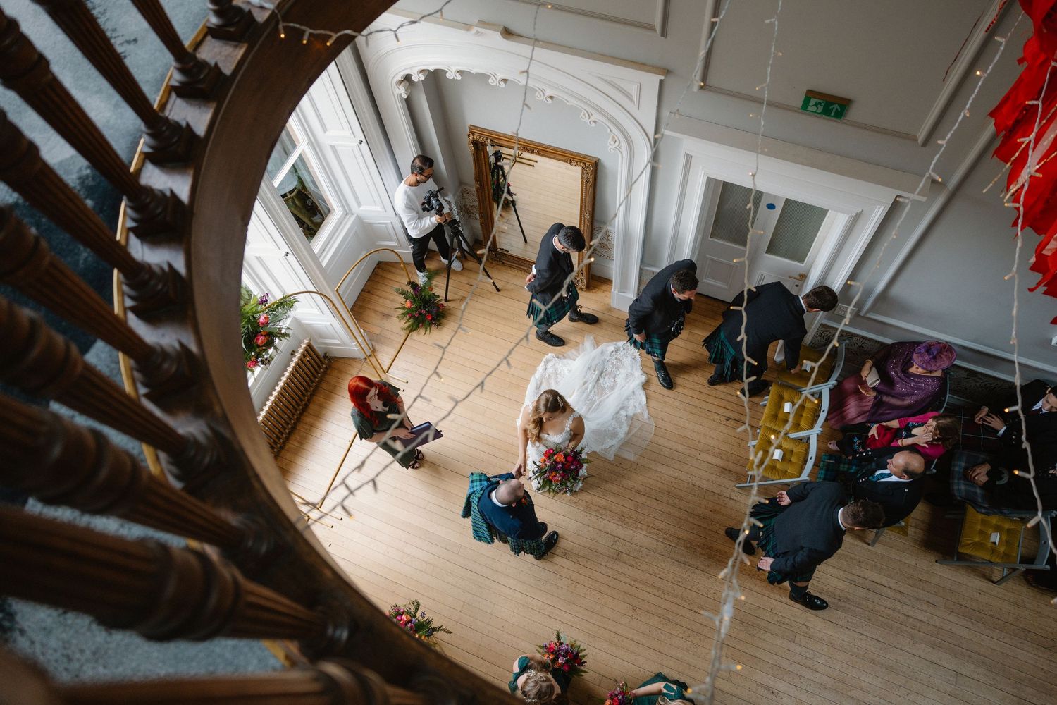 Aerial view of wedding ceremony preparations in a grand hall with spiral staircase and wooden floors.