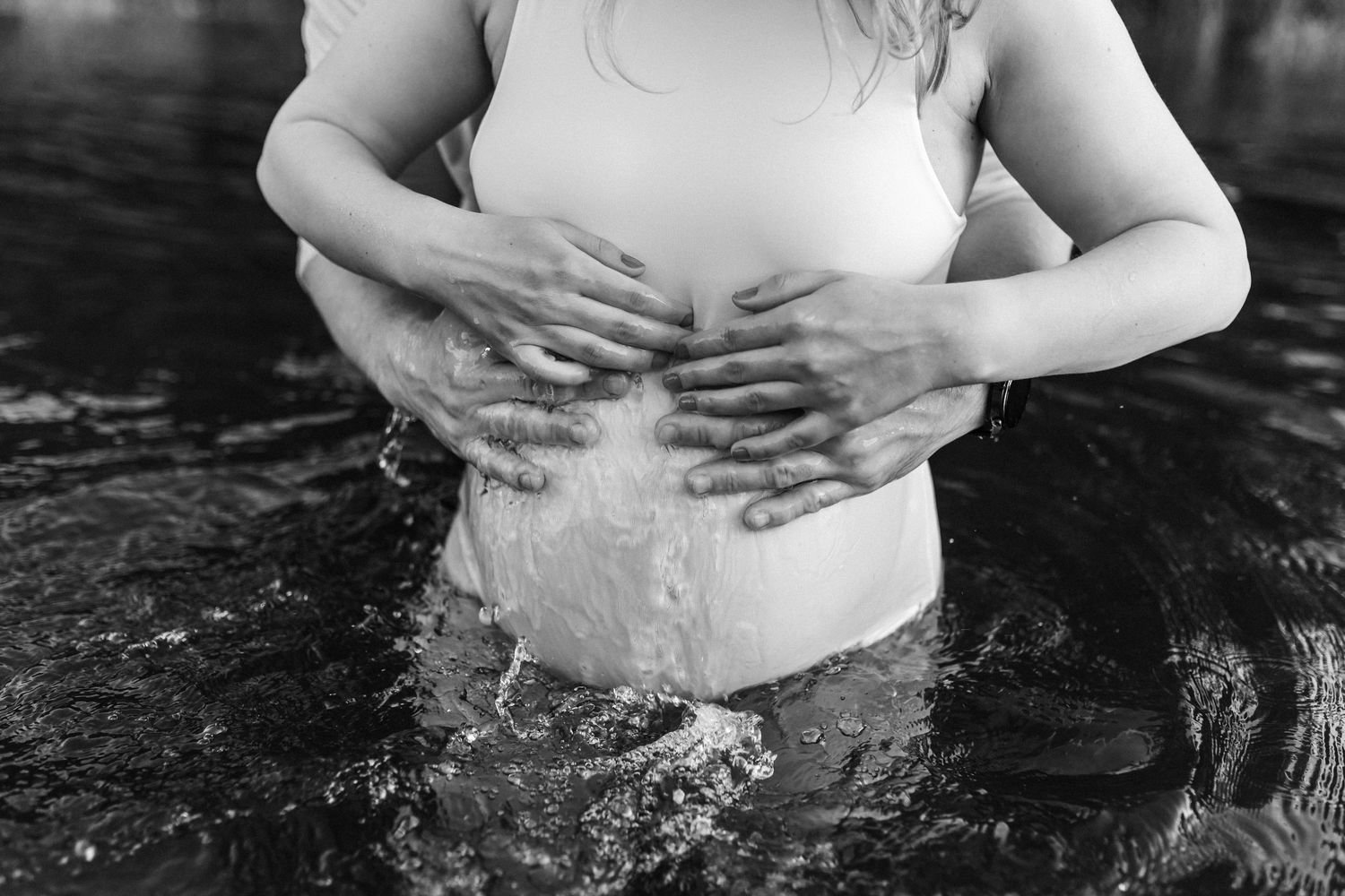 Black and white photo of hands on a pregnant belly while standing in water.