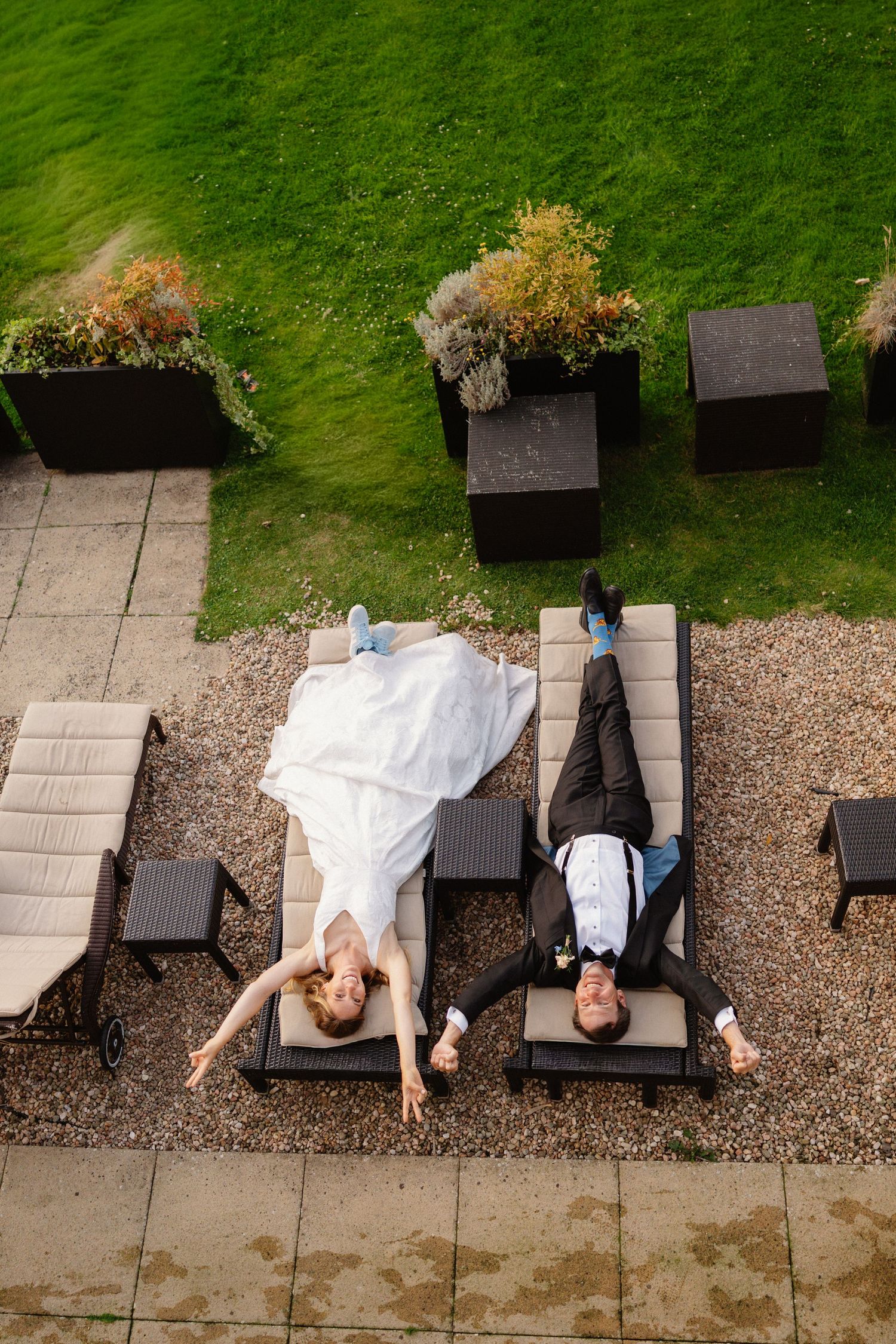 Aerial view of a bride and groom relaxing on lounge chairs in a garden patio after their wedding ceremony.