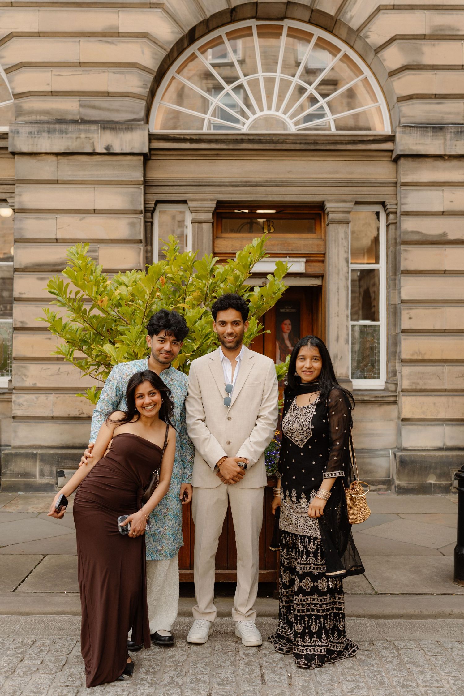Four wedding guests posing in formal attire outside a grand Georgian building with arched window in Edinburgh.