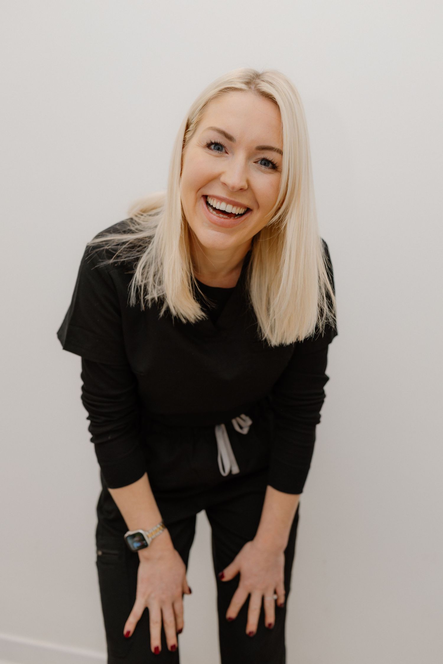 Healthcare worker in black outfit bending forward in clinical setting.