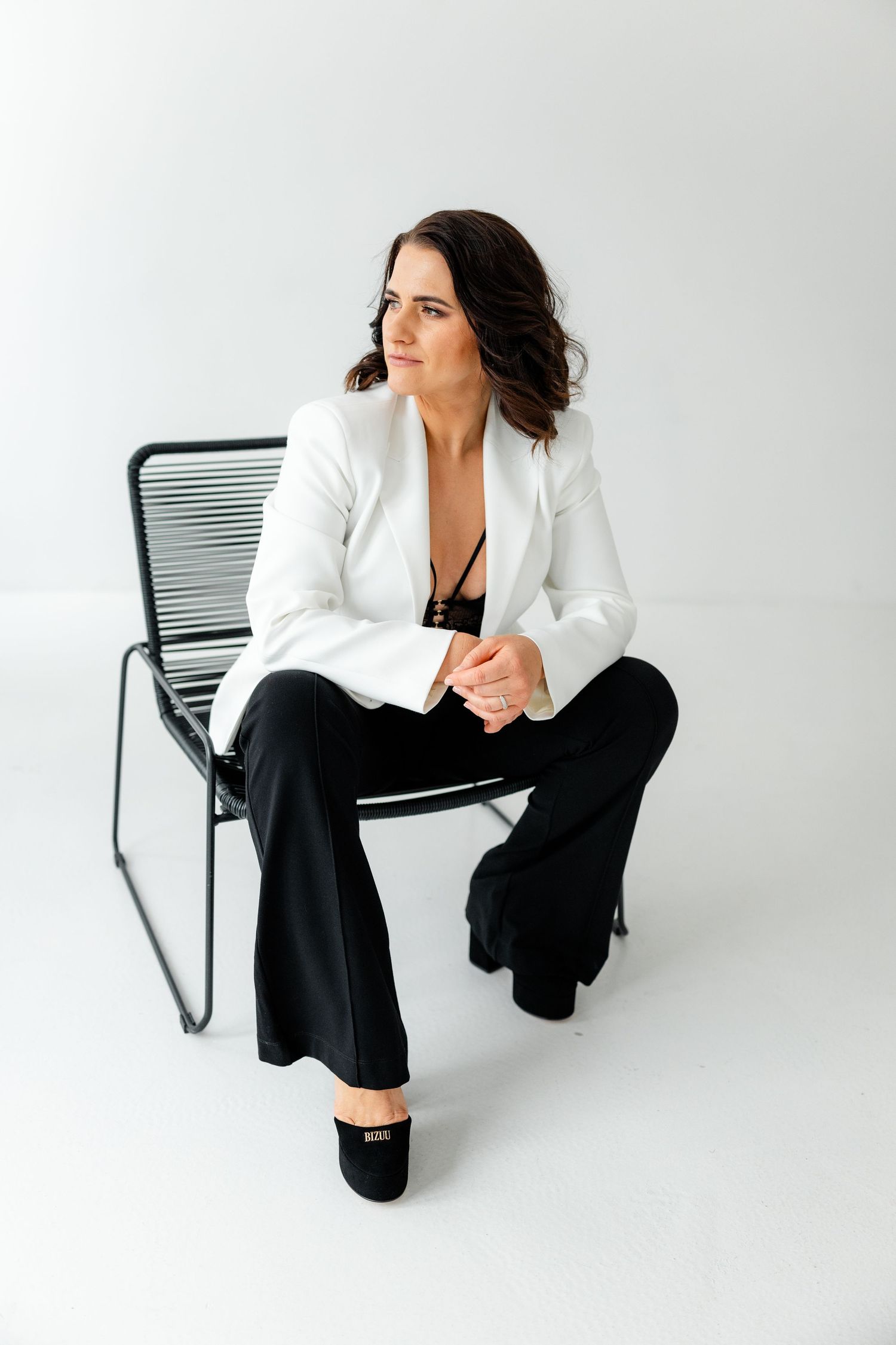 Professional portrait session with model in white blazer and black pants seated on modern chair.