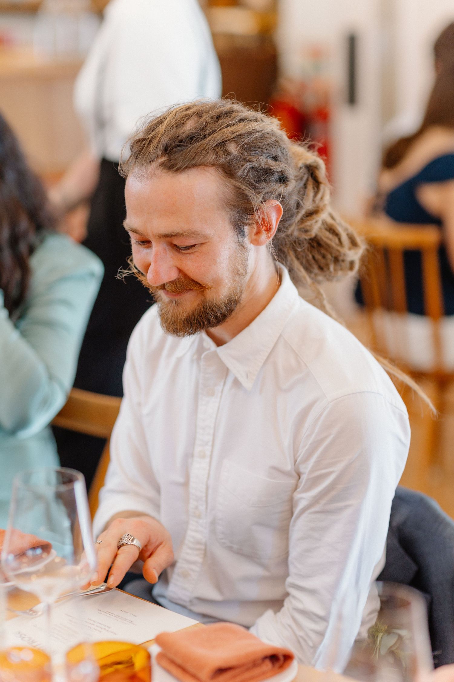 A person in a white button-down shirt sitting at a table during a social gathering.