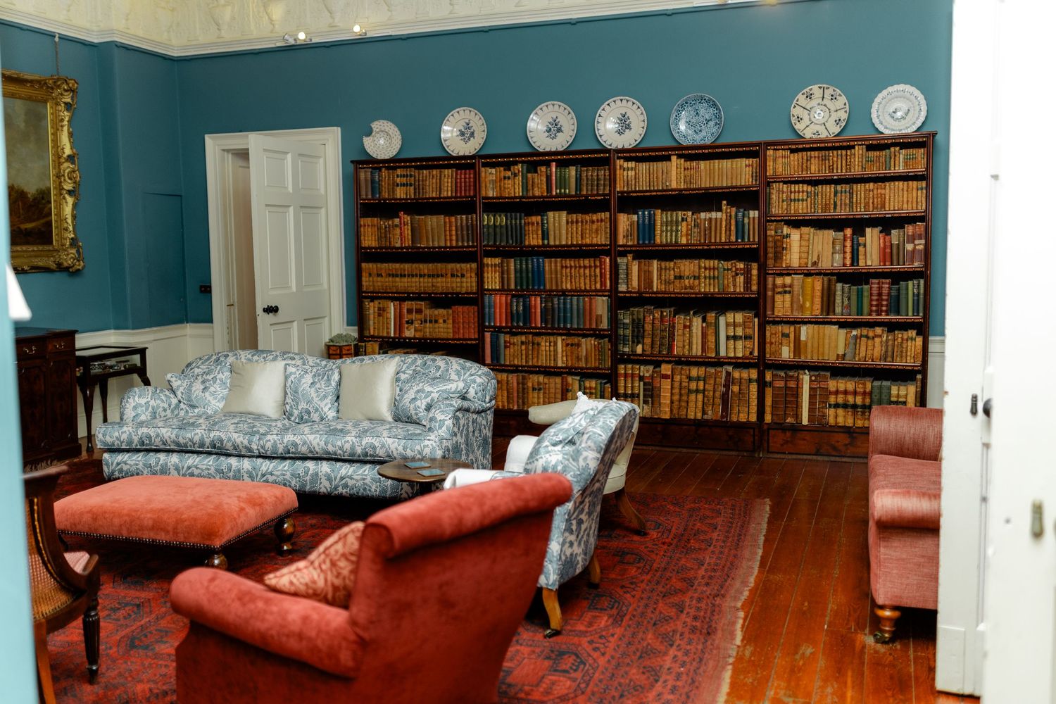 Library room with teal walls featuring built-in bookshelves and red upholstered furniture.