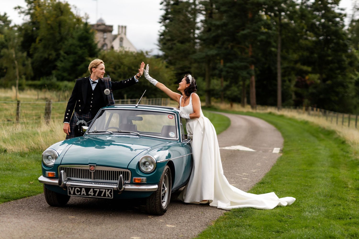 A couple celebrates by their vintage MG sports car on a winding country road.