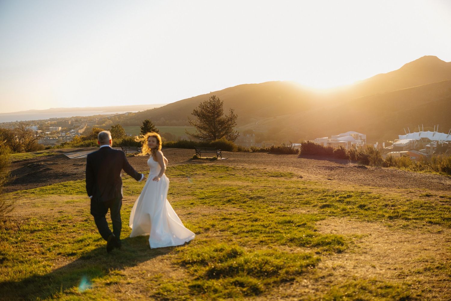 Sunset wedding photography in a golden field with mountains visible in the distance.