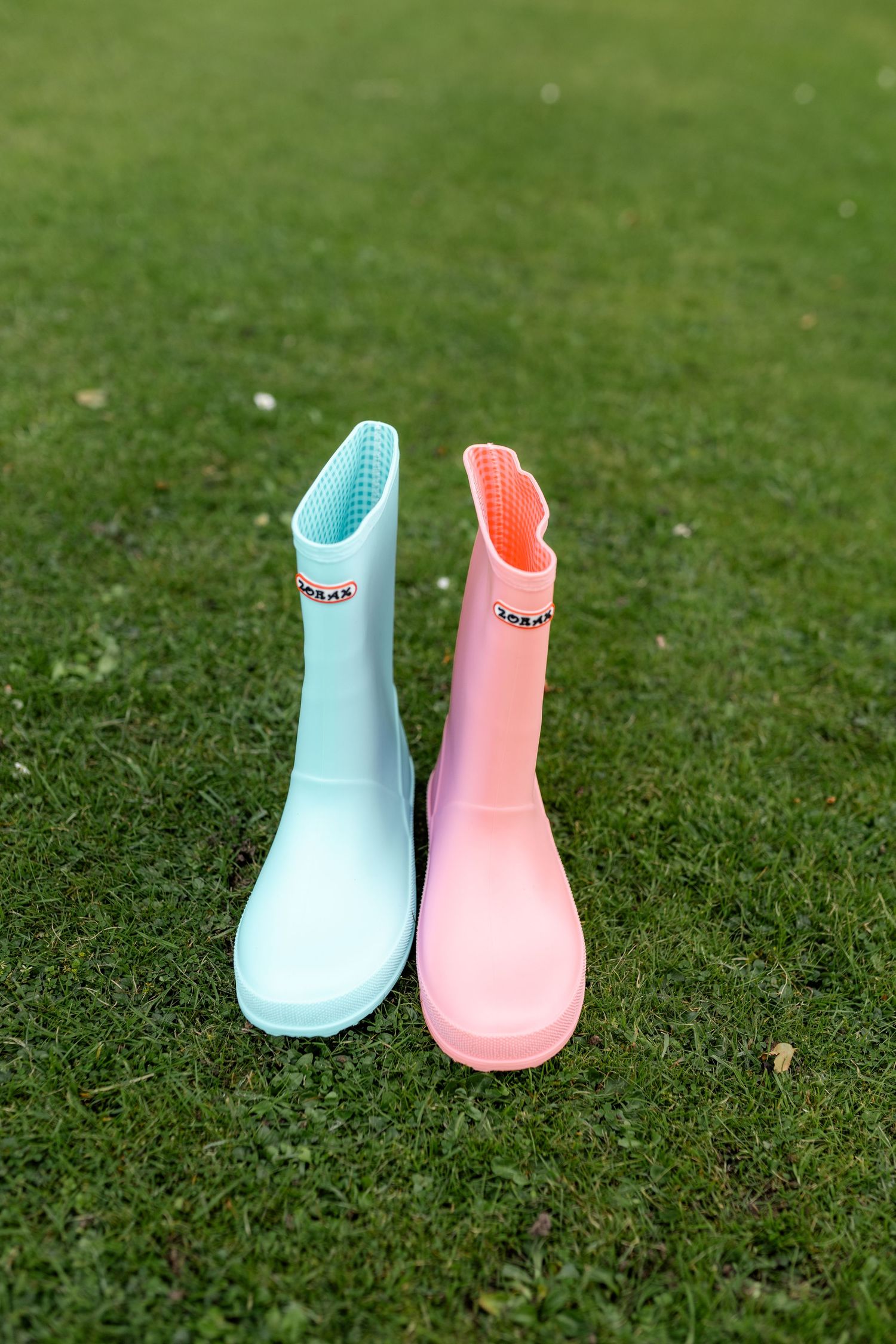 Pair of pastel mint and pink Hunter rubber rain boots standing on green grass.