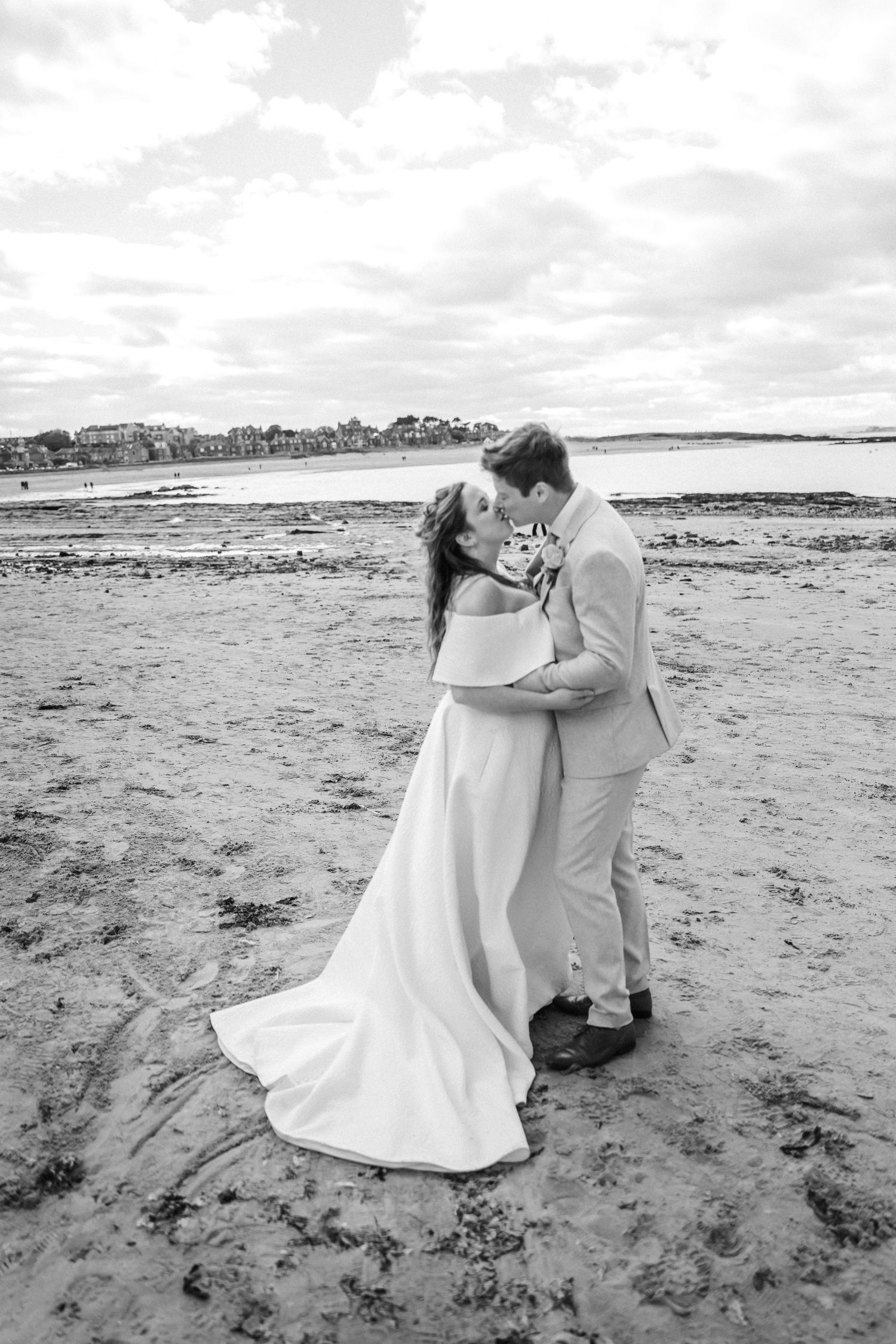 Bride and groom share a romantic kiss on a sandy beach in black and white wedding photo.