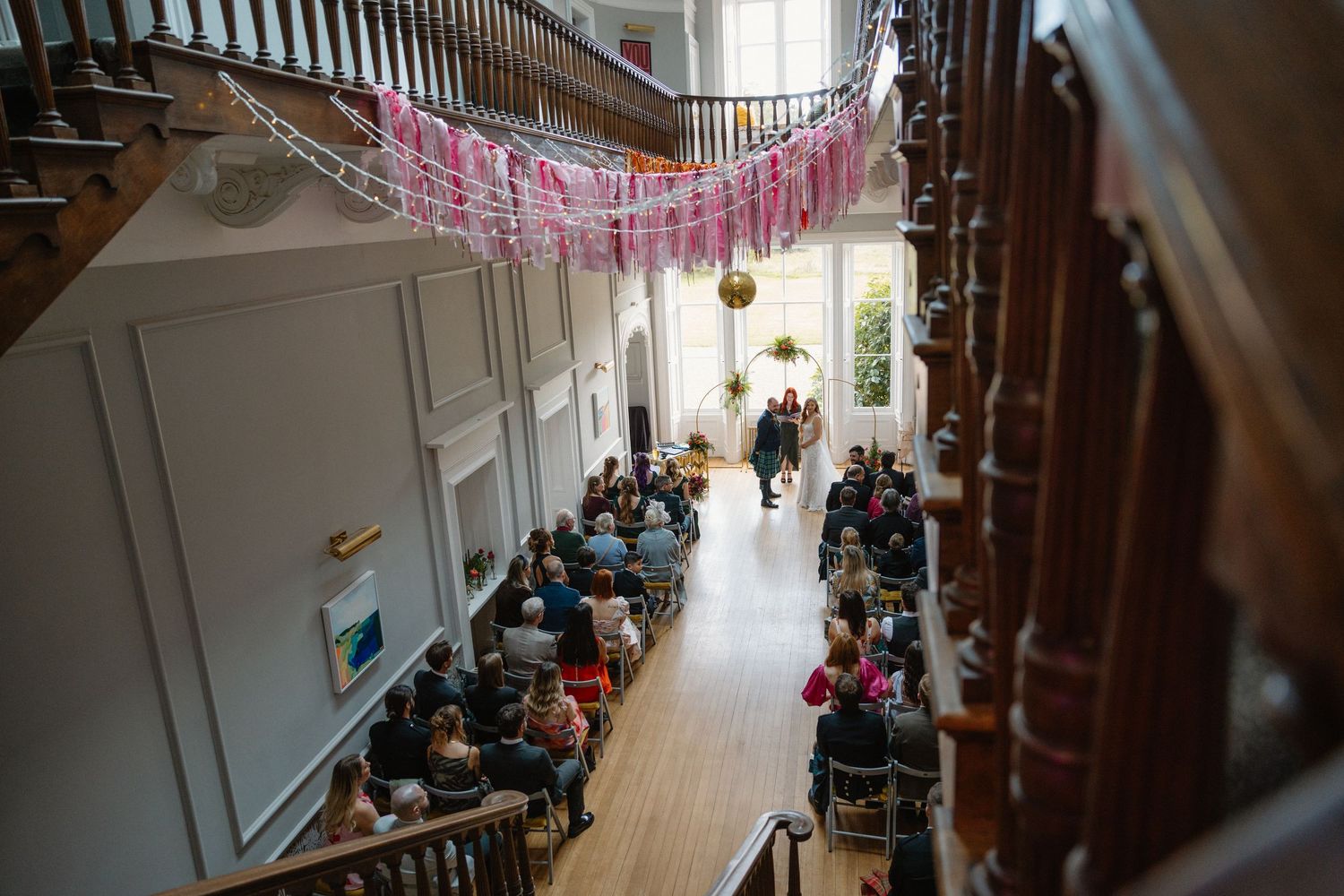 Overhead view of wedding ceremony guests seated in an elegant venue with pink decorations.