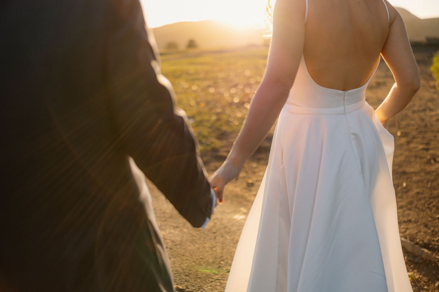 A couple holding hands at sunset in a white dress and black suit.