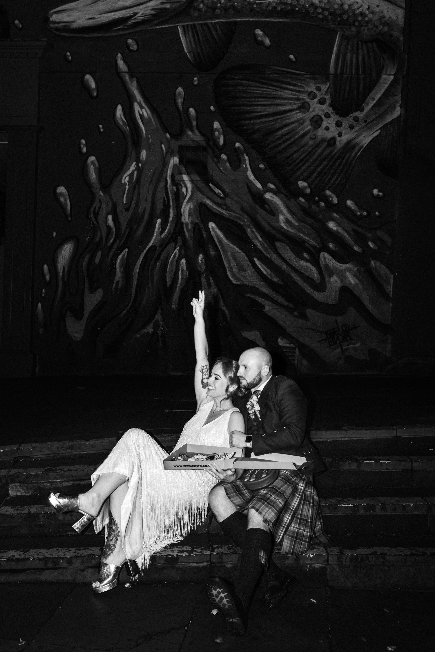 Artistic black and white photo of couple posing against dark wall with dramatic lighting.