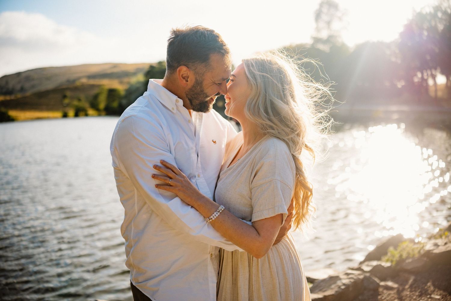Romantic couple embraces by a lake during golden hour sunset.