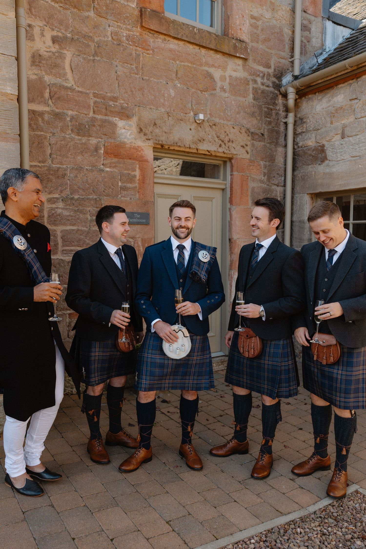 Groomsmen in traditional Scottish kilts and formal wear posing together.