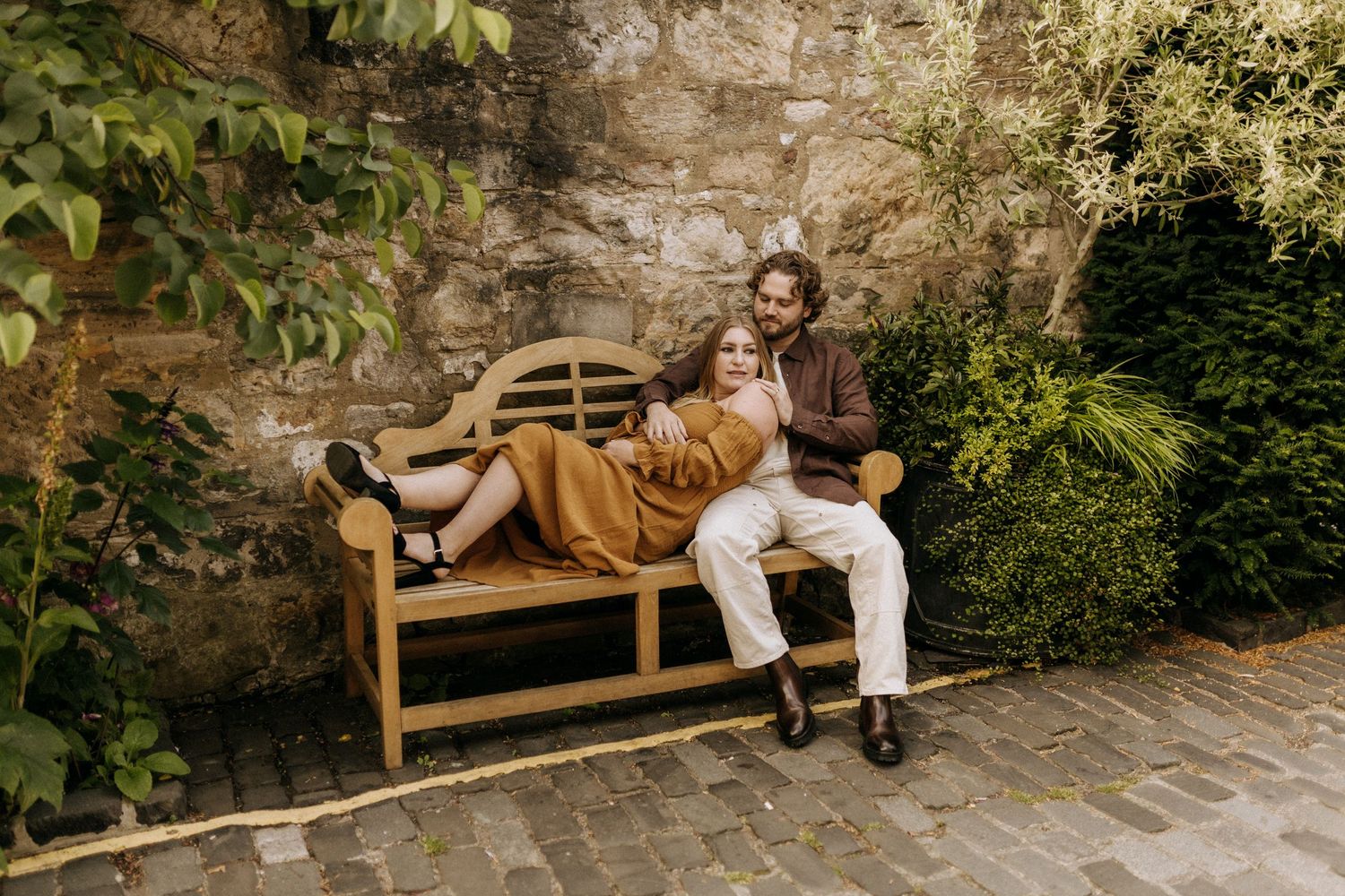 A couple relaxes on a wooden bench in a garden setting.