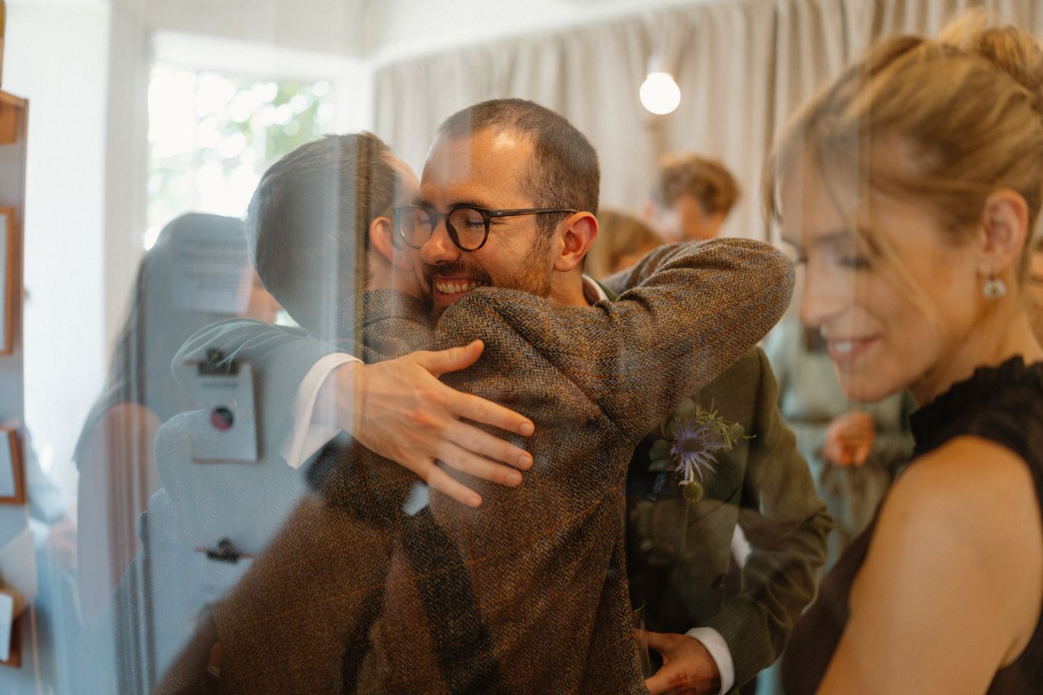 Groom in green suit shares warm hug with guest at intimate wedding reception celebration.