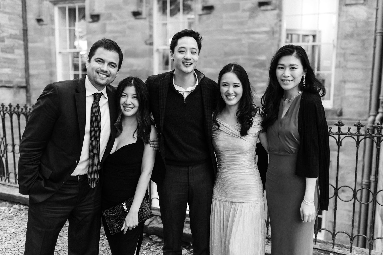 Group photo of wedding guests in formal attire standing outside a stone building.