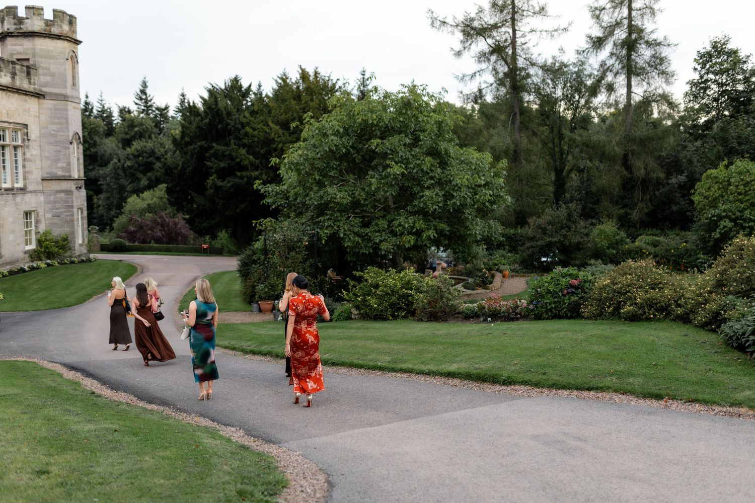 Groups walking along a curved path near a historic stone building surrounded by greenery.