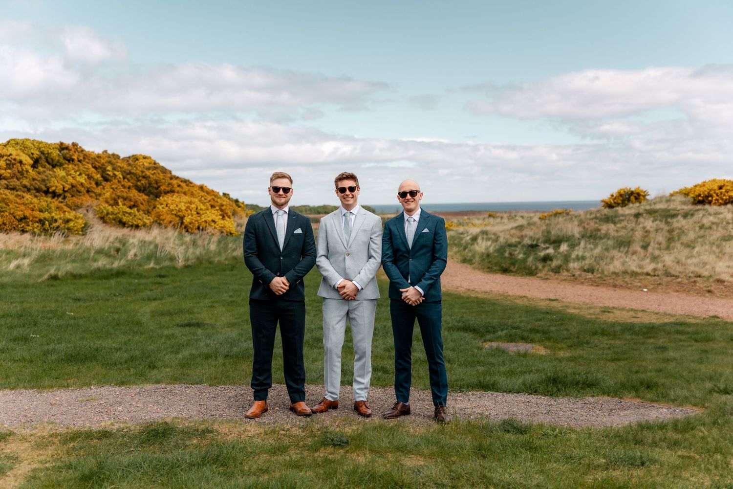 Wedding party poses against scenic coastal landscape with yellow gorse bushes.