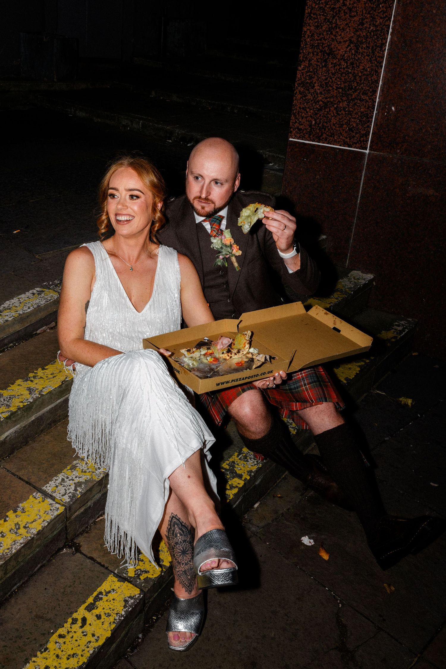 Newlyweds sitting on curb enjoying late night pizza together.