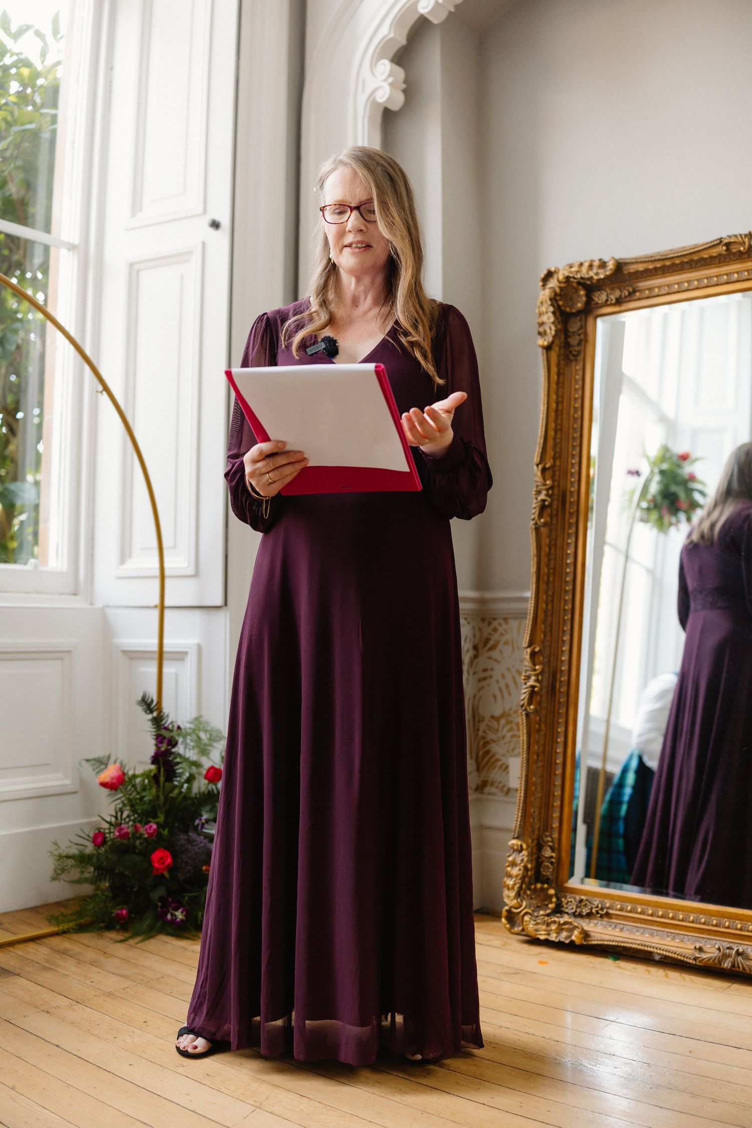 Wedding dress displayed in an elegant room with ornate gold mirror and hardwood floors.