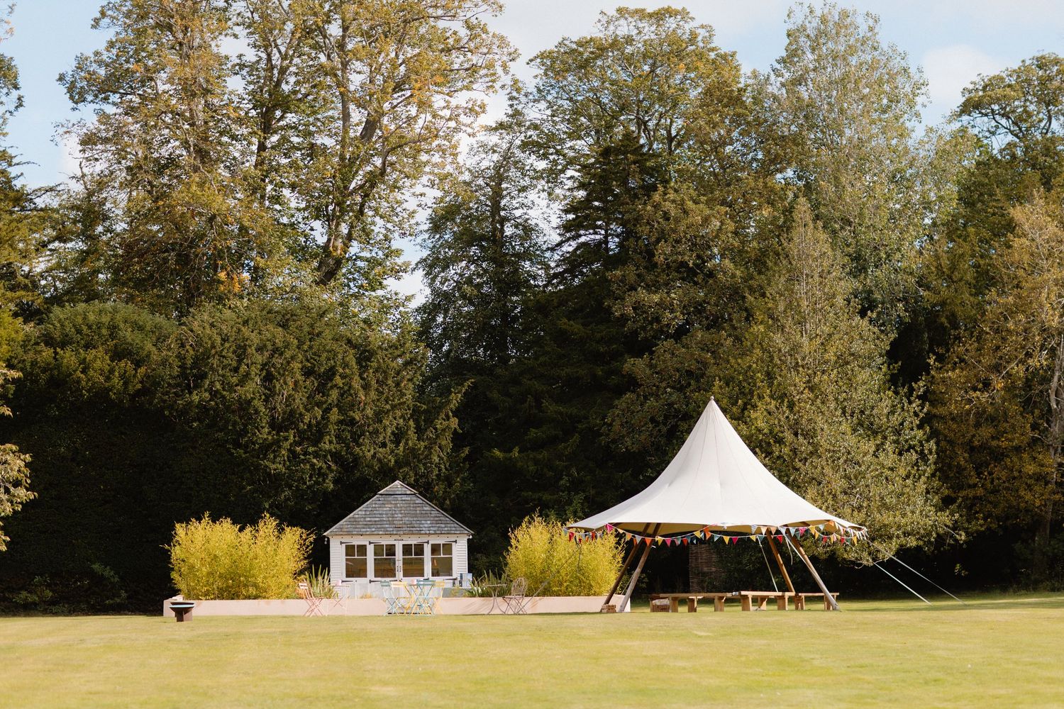 Panoramic view of a grassy field with autumn trees and a white tent pavilion in a park setting.
