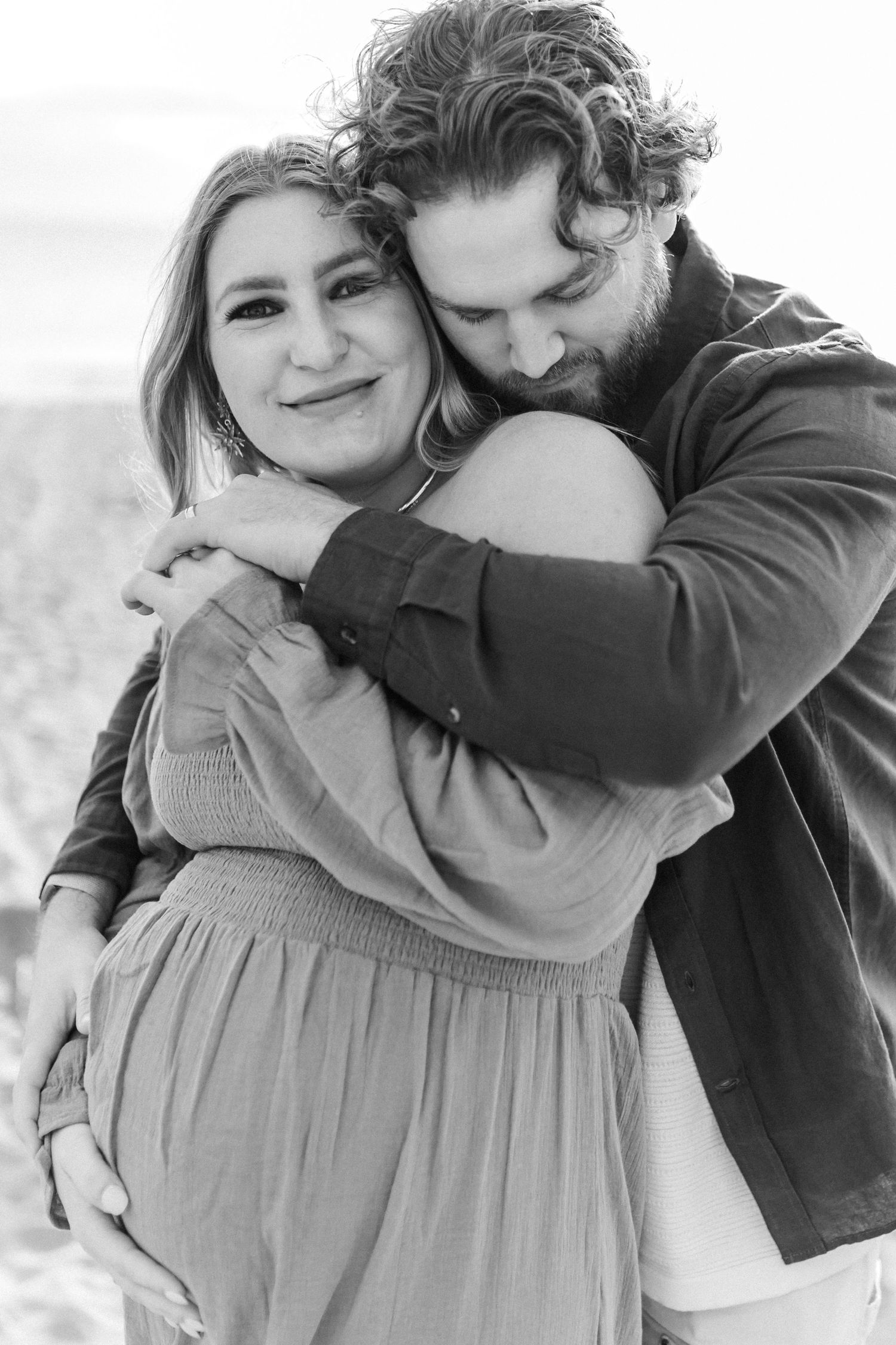 A romantic black and white portrait of a couple embracing outdoors with soft natural lighting.