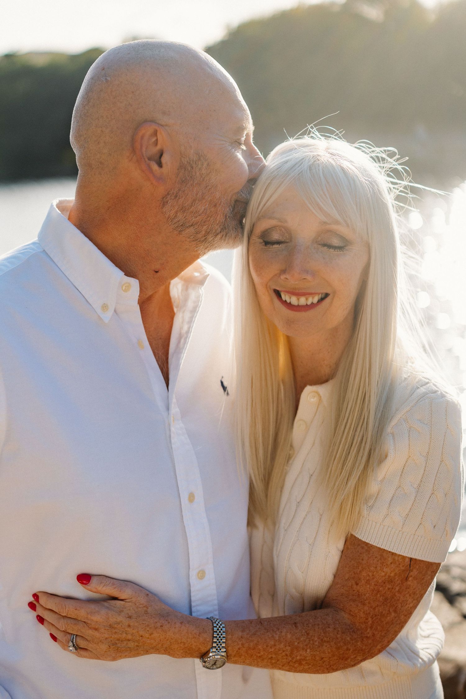 Intimate sunset portrait of a couple in white clothing embracing outdoors.