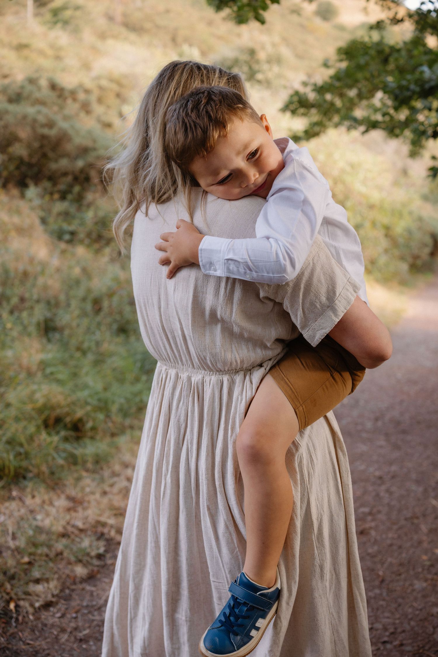 Mother and child share tender moment in white dresses on nature path.