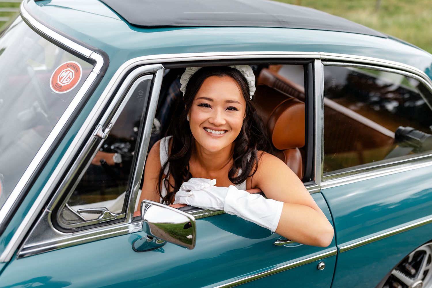 A vintage teal MG sports car interior view through the driver's window.