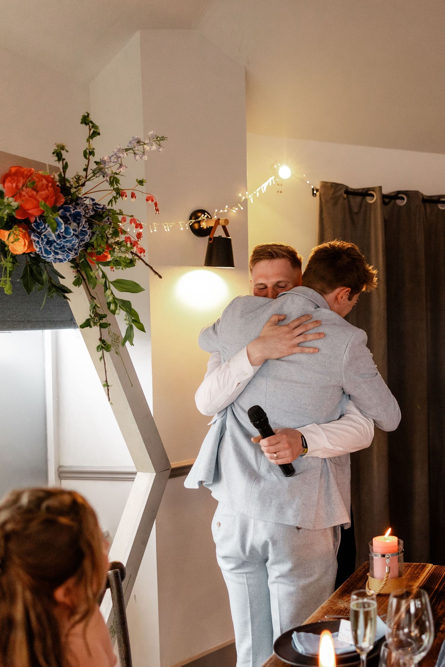 Emotional embrace between people in light grey suits during a wedding reception.
