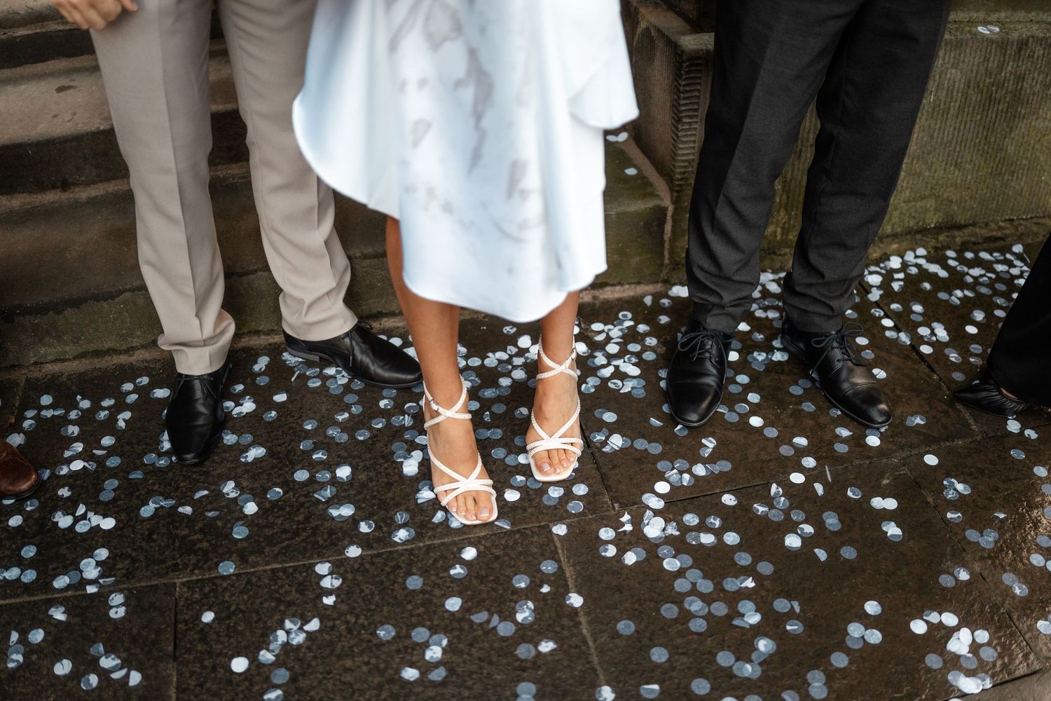 White heels and confetti scattered on dark stone ground at wedding celebration.