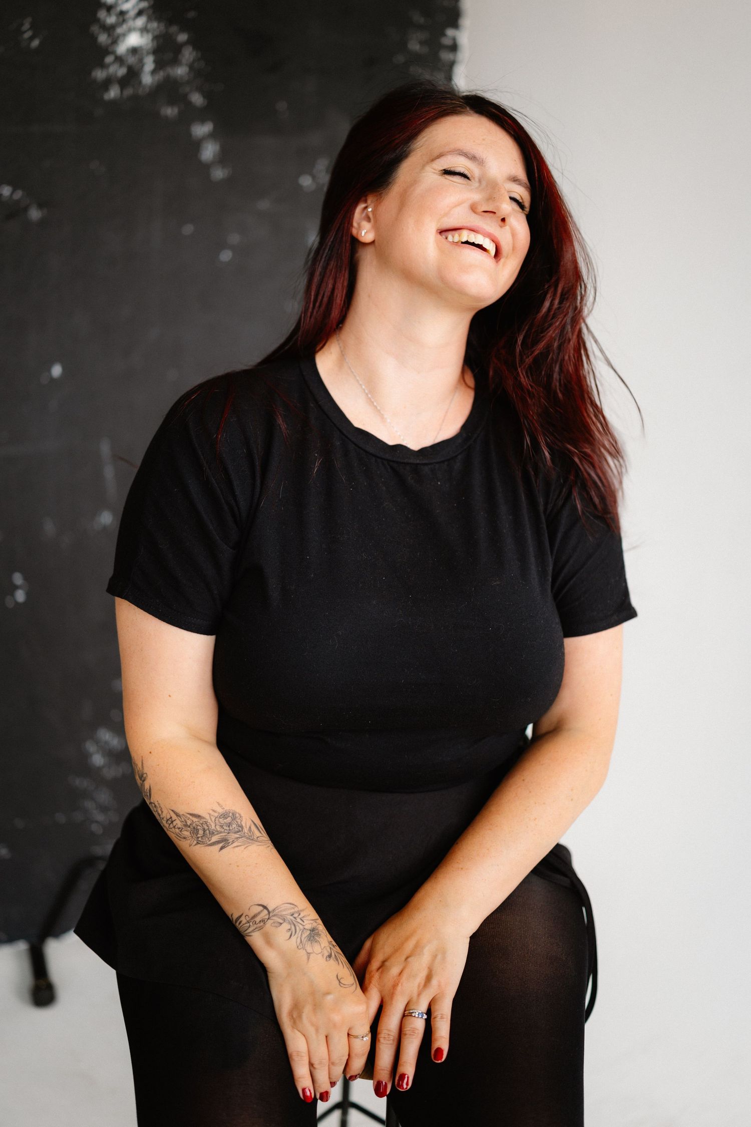 Portrait of person in black shirt laughing against dark background.