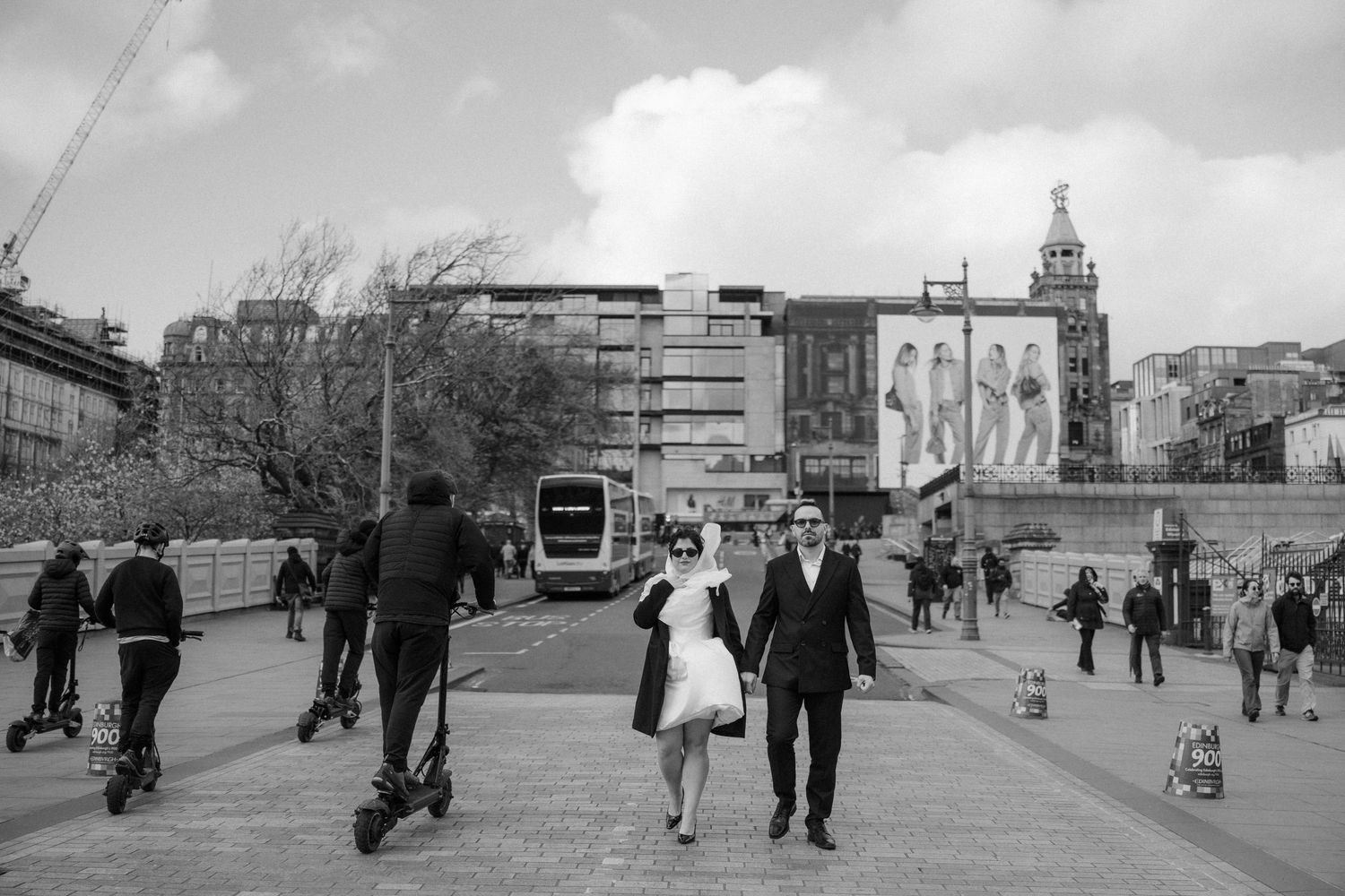 Bride and groom walking across a busy urban plaza in black and white wedding photo in city center.