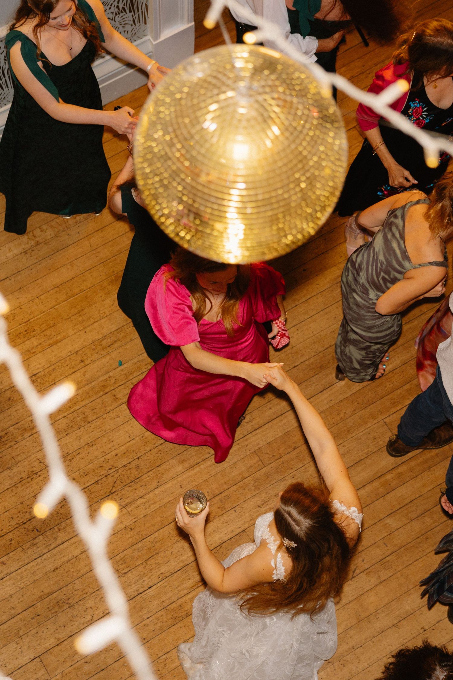 Aerial view of bride and guest dancing under a gold disco ball at wedding reception.