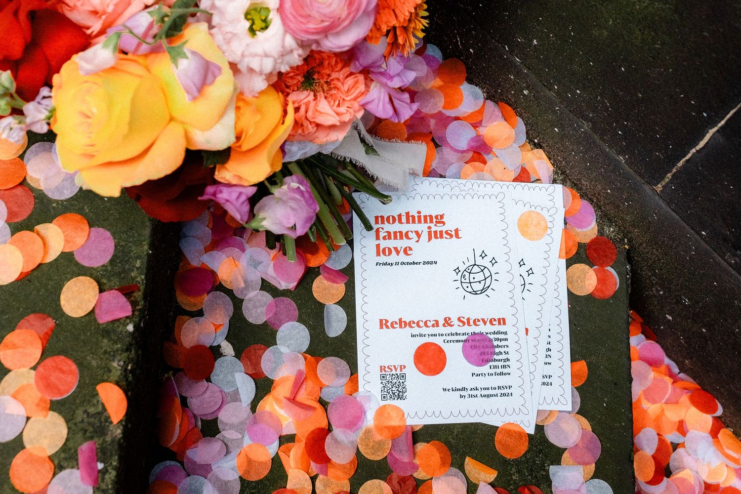 Colorful wedding invitation reading nothing fancy just love for Rebecca and Steven surrounded by confetti and flowers.