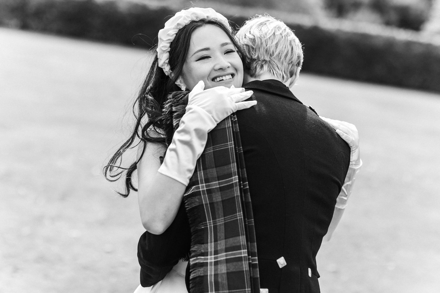 Bride smiling and hugging groom in tartan kilt at Scottish wedding, black and white photo.